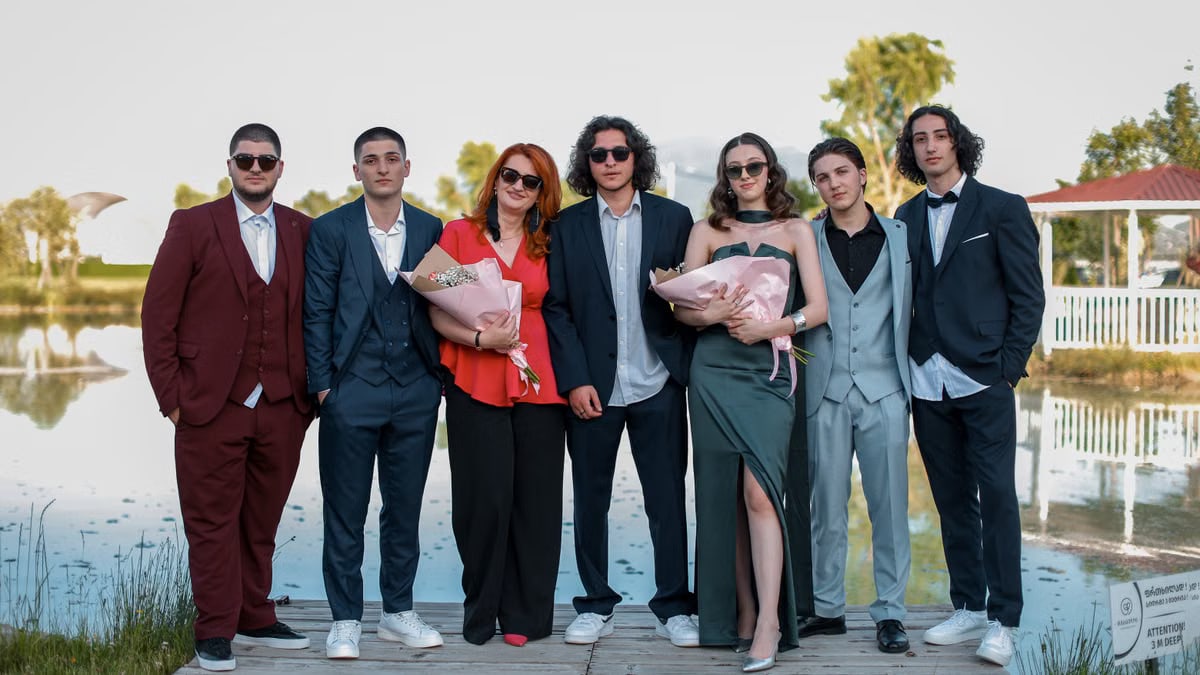 A group of people dressed formally celebrating outdoors by a lakeshore.